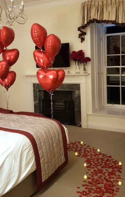 Room decorated with romantic Red heart balloons,red roses, Tea light candles and rose petals
