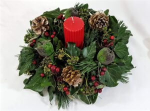 A round Christmas Flowers with mixed greens, pinecones and red candle in the centre