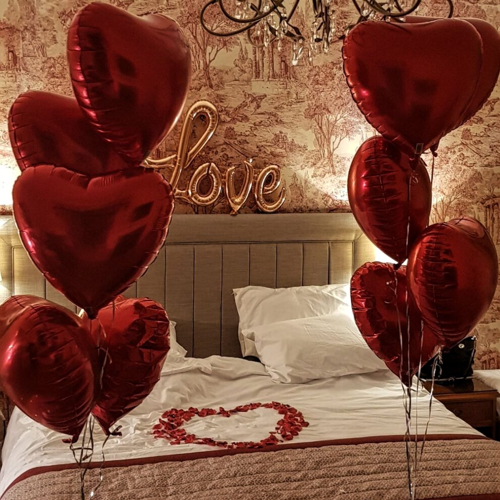 Bed decorated with red rose petals and Red Heart Balloons